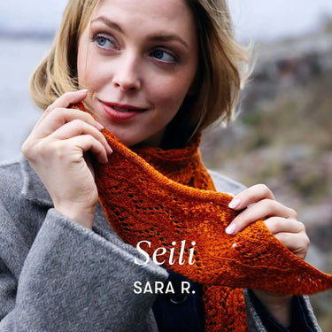 Woman wearing and admiring an orange knitted scarf from Archipelago Knitting collection