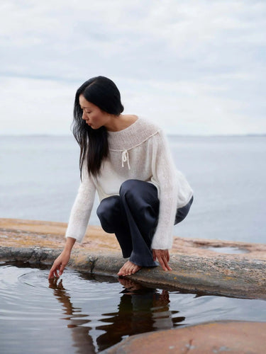 Woman wearing knitwear inspired by Art of the Sea on a rocky shoreline.