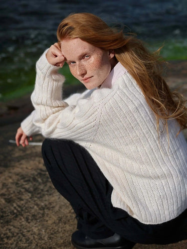 Art of the Sea knitwear design inspired by the Moomins, featuring a cozy, white sweater modeled outdoors by the water. Pre-order now.