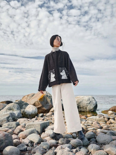 Model wearing knitwear from Art of the Sea - 23 Knitwear Designs Inspired by the Moonins, standing on a rocky beach.