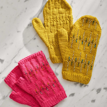 Yellow mittens and pink fingerless gloves showcasing Beaded Colourwork knitting design on marble surface.