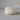 A small ball of soft off-white yarn resting on a textured light fabric surface, with a softly blurred neutral background and dried floral decor in the upper right.