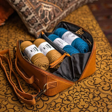 Brown leather bag with yarn rolls on a patterned fabric background