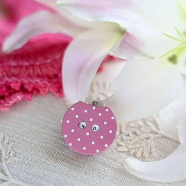 Pink polka-dot Row Counter with push button by KnitPro, resting on a floral background.