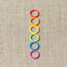 Cocoknits Round Stitch Markers in rainbow colors on a beige surface, perfect for knitting projects.