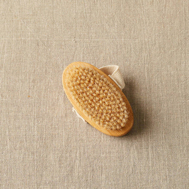Cocoknits Sweater Care Brush with natural boar bristles for textile rejuvenation on a linen backdrop.