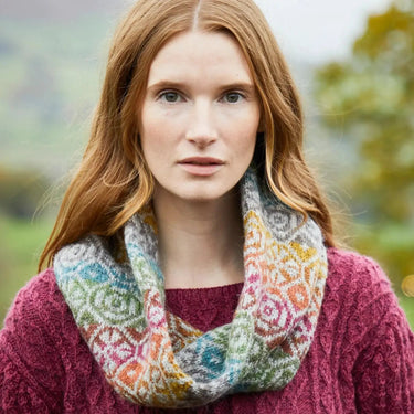 Woman wearing colorful Ennerdale Cowl Kit by Marie Wallin, featuring intricate Fairisle knitting, in an outdoor setting.