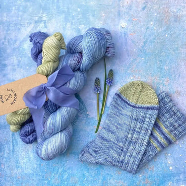 Yarn Knitting kits by Ainsworth & Prin featuring blue and green yarn skeins with matching knitted socks and a silk ribbon.