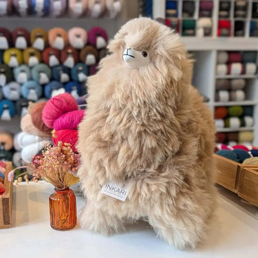 Stuffed Alpaca animal by Inkari in a cozy yarn shop, showcasing fluffy texture and beige color.