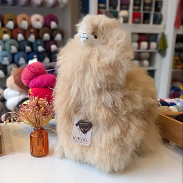 Soft and cuddly Inkari Stuffed Alpaca Animal on display, surrounded by colorful yarns and decor.