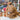Inkari Stuffed Alpaca Natural size displayed on a shop counter with colorful yarn background