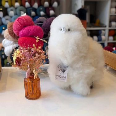 Inkari Stuffed Alpaca Animal in a cozy setting with colorful yarns and dried flowers.
