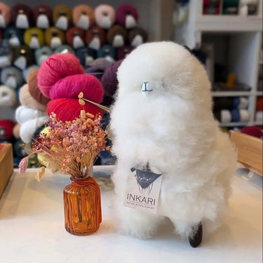 Stuffed Alpaca toy from Inkari, displayed with yarn and dried flowers, showcasing the soft and adorable design of the plush animal.