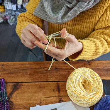 Person learning knitting in Beginner Knitting Class with yellow yarn.
