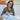 Woman with glasses holding fabric in a room with colorful abstract art on the wall.