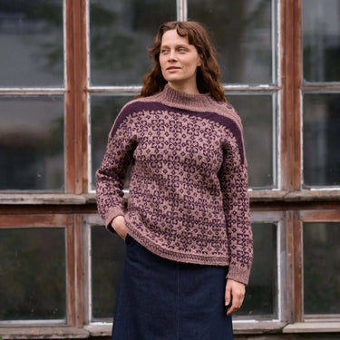 Woman wearing a patterned sweater and dark skirt standing in front of an old building with large windows.