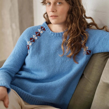 Woman wearing a blue sweater with floral patterns sitting on a couch.