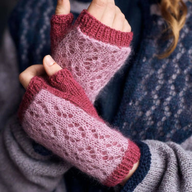 Close-up of pink and red knitted fingerless gloves held by a person wearing a blue sweater.
