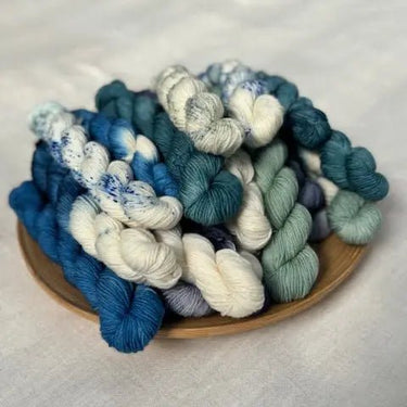 Mini skeins from the Kokon Blue Knit Me An Ocean Yarn Advent Calendar displayed on a wooden plate.
