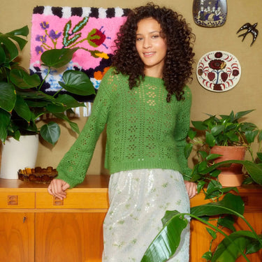 Model wearing green crochet sweater from Let's Crochet Issue 2 by Laine with vibrant decor and plants.