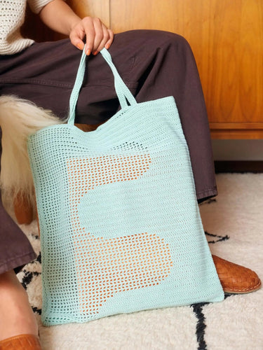 Hand holding a light blue crochet tote bag with a unique design, featured in Let's Crochet Issue 2 by Laine.