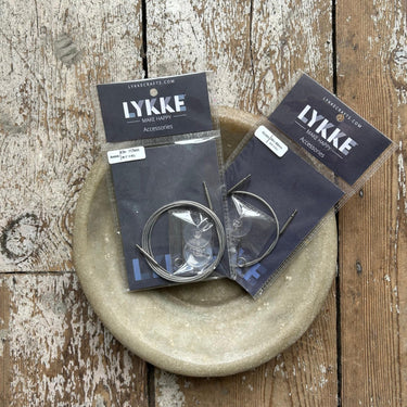 Two packages of LYKKE knitting needle cables on a rustic wooden surface