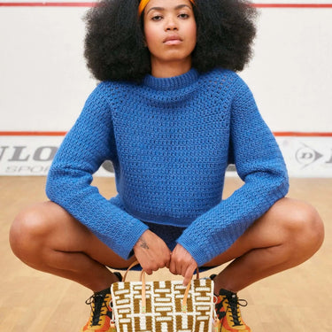 Person wearing blue crocheted sweater holding a patterned bag. Showcasing design from Hooks Out! by Molla Mills.