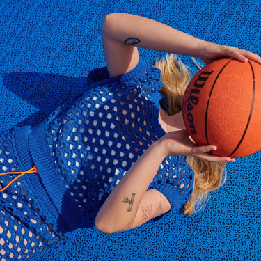 Person in crocheted outfit holding basketball, showcasing Hooks Out by Molla Mills, vibrant blue design on patterned surface.