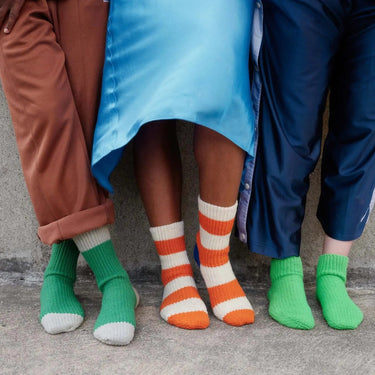 Colorful socks with striped patterns worn by three people, showcasing playful and vibrant fashion on a concrete surface.