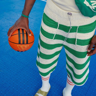 Person wearing green and white striped crochet shorts holding a basketball, featuring a design from Hooks Out by Molla Mills.