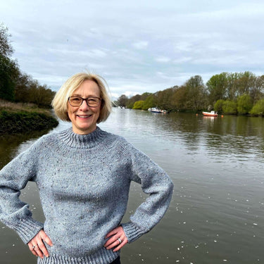 Woman wearing a knitted jumper by a river, promoting My First Knitted Jumper Workshop.