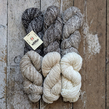 Four skeins of Noro Haunui Silk yarn in natural shades of gray and brown, made from raw mulberry silk and Haunui merino wool.
