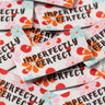 Embroidered patches with 'IMPERFECTLY PERFECT' text and floral designs on a pile.