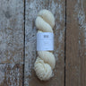 A skein of cream-colored yarn with a white paper label, placed vertically on a rustic, weathered wooden plank surface.
