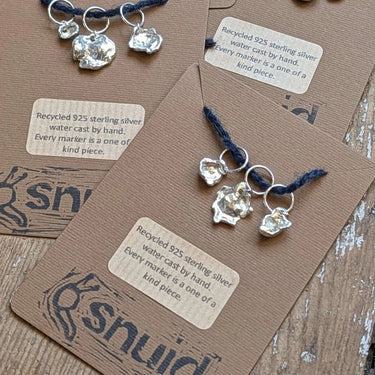 Handcrafted Silver Stitch Markers by Snuid made from recycled 925 silver with unique organic shapes, displayed on eco-friendly packaging.