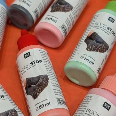 Sock Stop - NonSlip Socks rubber milk bottles for DIY non-slip soles on slippers, displayed in various colors on an orange background.