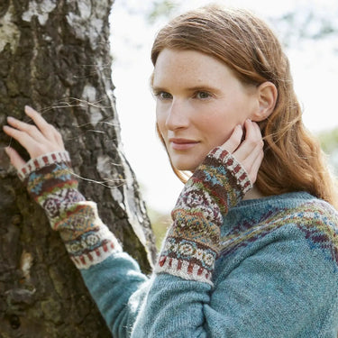Woman wearing Sycamore Armwarmers Kit by Marie Wallin in colorful woolen design, leaning against a tree for Wildwood collection photo.