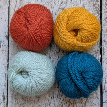 Four balls of yarn in orange, yellow, light blue, and dark blue on a wooden background, perfect for crochet projects.