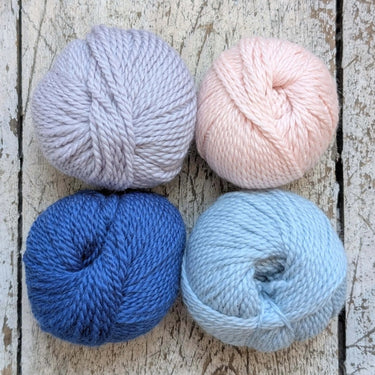 Four balls of yarn in pale pink, lavender, deep blue, and light blue on a rustic wooden surface.