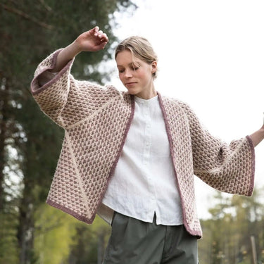 Woman wearing a patterned cardigan in a natural setting with trees. Tukubook knitting book