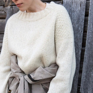 Person wearing a white knitted sweater from the Tukubook collection, showcasing Finnish knitting design with subtle textures. Tukubook knitting book