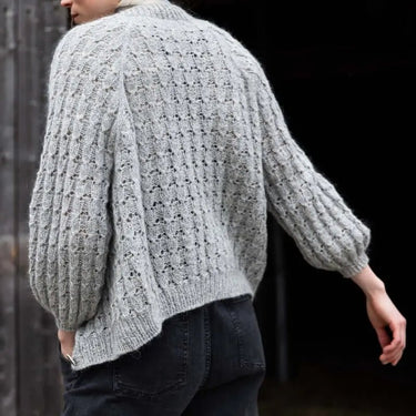 Person wearing a textured gray sweater against a wooden fence background Tukubook knitting book