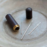 Dark brown wooden case with metal darning needles displayed on a surface.